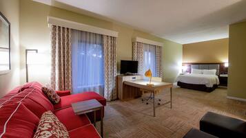 A hotel room with a red sofa, a desk with a computer, a bed, and a TV.