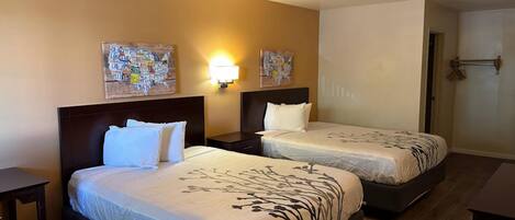 A hotel room with two beds, a nightstand, a wall-mounted lamp, and two wall art pieces.