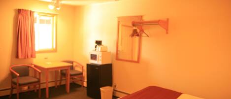 Een hotelkamer met een bed, een bureau met stoel, een magnetron en een kledingkast.