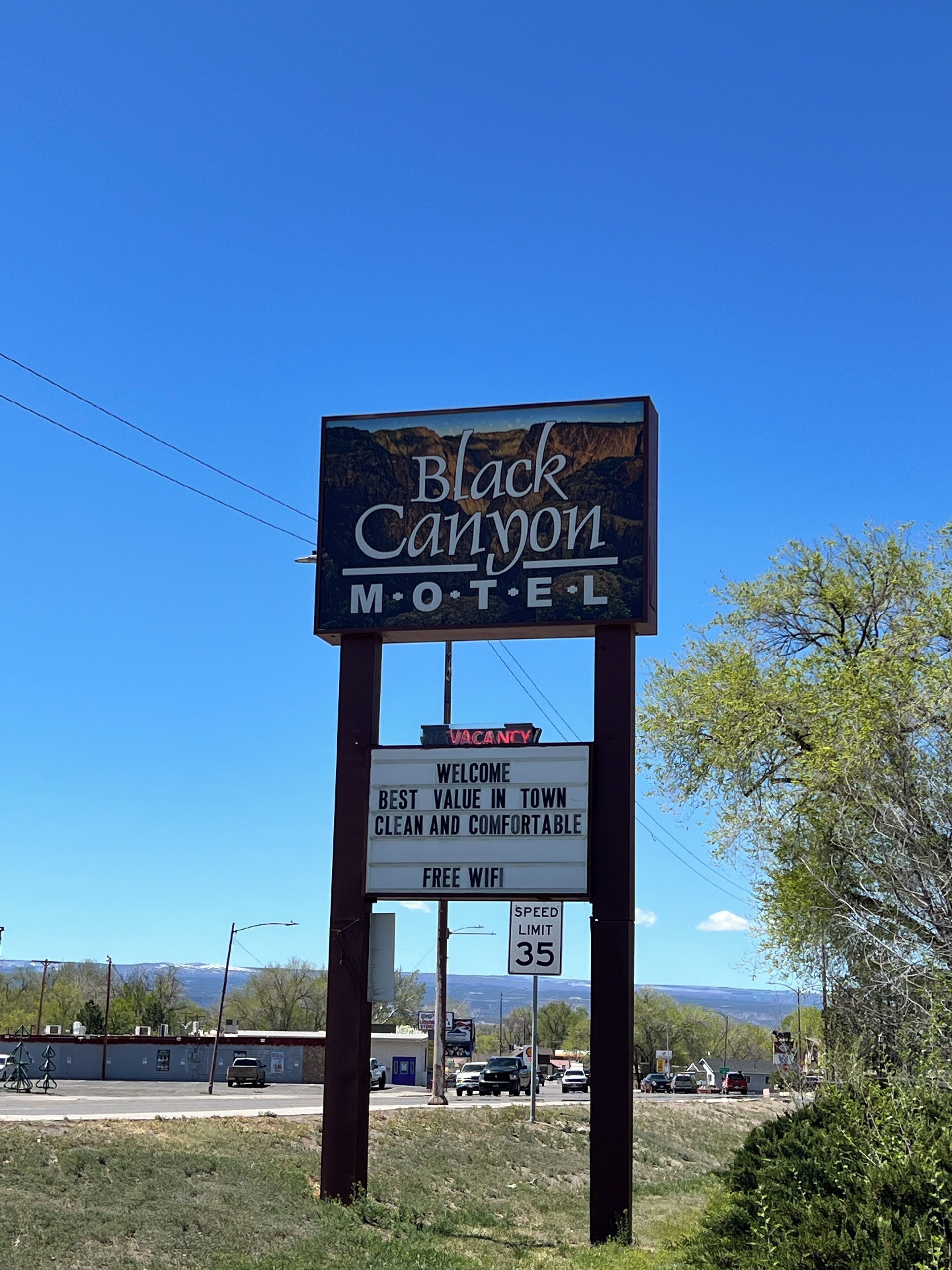 A motel sign with "Black Canyon Motel" and "VACANCY" text, a speed limit sign of 35, and a welcome message stating "Best Value in Town, Clean and Comfortable, Free WiFi".