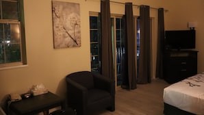 Quarto de hotel com cama, uma cadeira, escrivaninha com telefone, televisão e janela com cortinas.