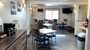 Uma sala de jantar moderna com várias mesas e cadeiras, um espaço para café e uma televisão fixada na parede.