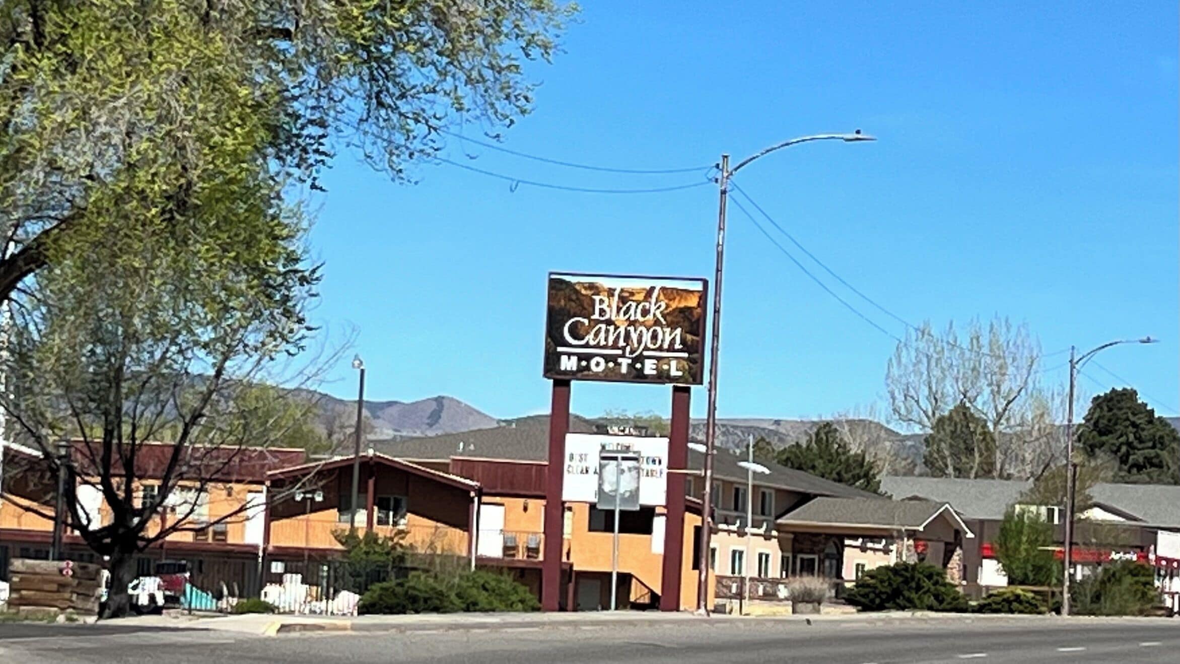 A motel named Black Canyon with a prominent sign, a parking area, and buildings in the background.