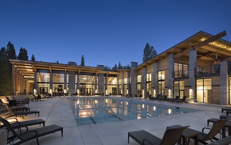 A modern hotel with a large outdoor pool, multiple lounge areas, and a covered patio.