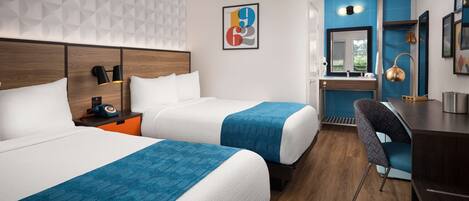 Quarto de hotel com duas camas, uma escrivaninha, uma cadeira e banheiro visível através de uma porta aberta.
