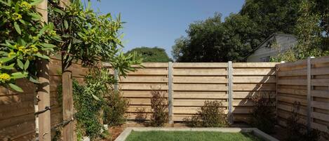 Patio trasero cercado con césped, valla de madera y diversas plantas.