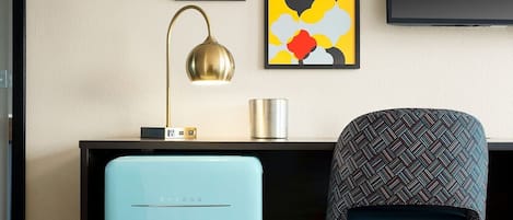 Una habitación moderna con un otoman azul, un escritorio con una lámpara y obras de arte en la pared.