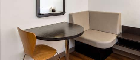 A corner room with a round table, a wooden chair, a beige sofa, and a mirror on the wall.
