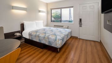 A hotel room with a bed, bedside table, and a window with a view of greenery.