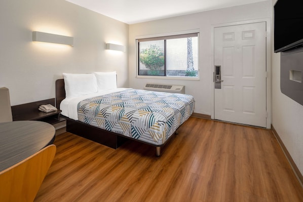 Habitación de hotel con cama, mesita de noche y ventana con vistas al verdor.