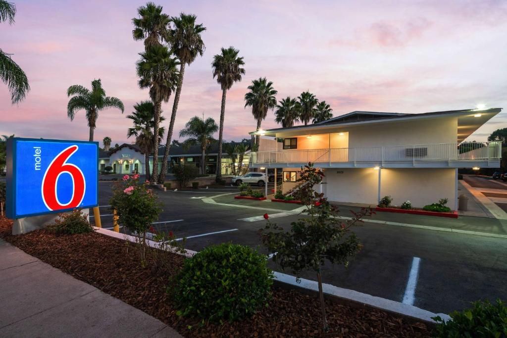 A motel with a large sign, a parking lot, and a building with a balcony.