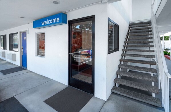 A modern building entrance with a 'welcome' sign, a glass door, and a staircase leading up. - Vagabond Inn Santa Barbara (Santa Barbara)