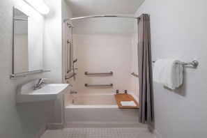 A bathroom with a sink, mirror, shower, and towel rack.