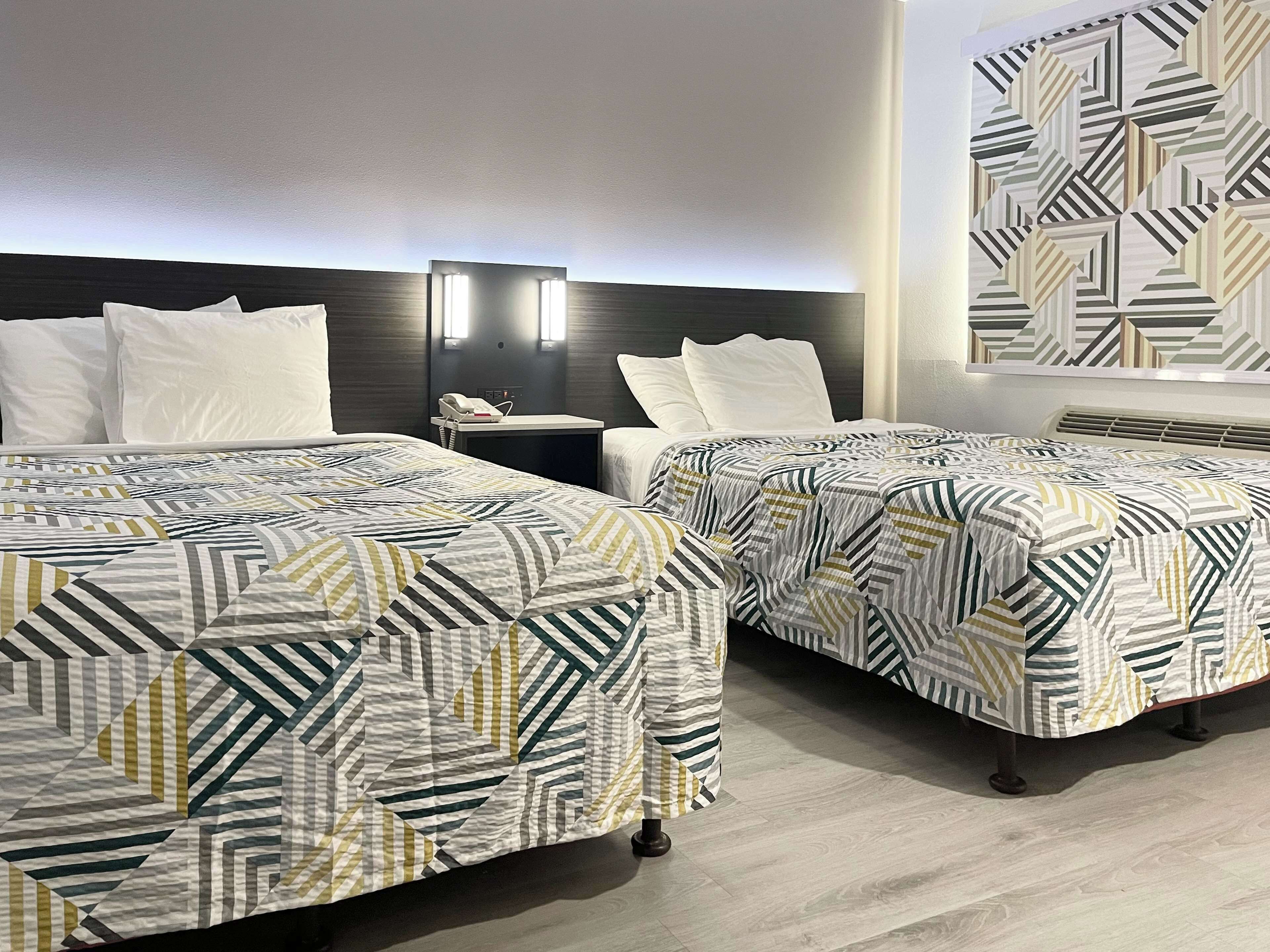 Une chambre d’hôtel avec deux lits, chacun agrémenté de draps à motifs, une table de chevet avec un téléphone et un luminaire fixé au mur.