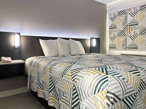 A modern hotel room with a large bed, a nightstand with a phone, and a geometric-patterned wall. - Motel 6 Morro Bay, CA (Morro Bay)