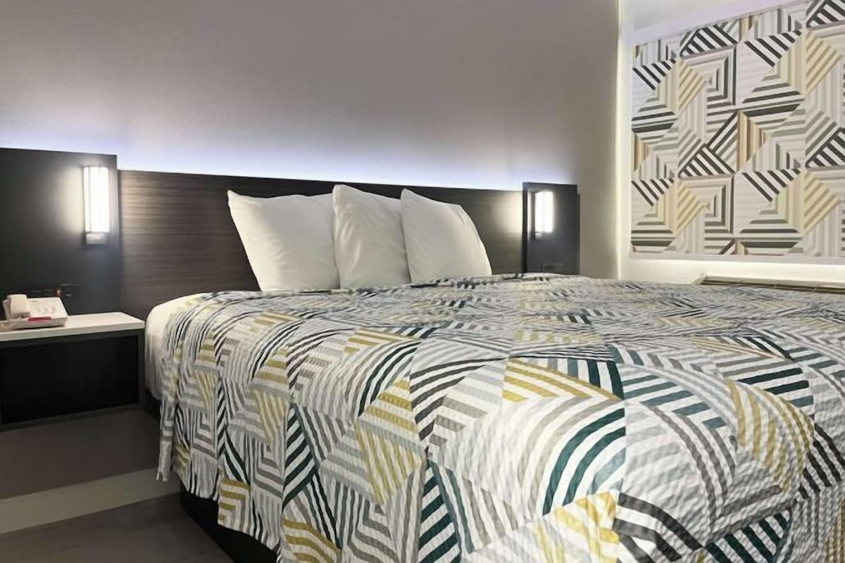 Habitación de hotel con una cama grande, una mesita de noche y una lámpara fijada a la pared.