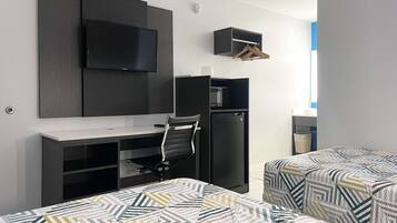 A hotel room with a desk, chair, TV, wardrobe, and two beds with patterned bedding.