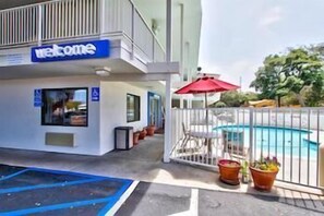 Ein Hotel mit einem 'Welcome'-Schild, einem Poolbereich und einer umzäunten Terrasse mit Pflanzkübeln.