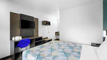 A hotel room with a bed, a desk with a chair, a TV mounted on the wall, and a wardrobe.