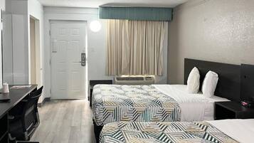 A hotel room with two beds, a desk, a chair, a door, and a window with curtains.