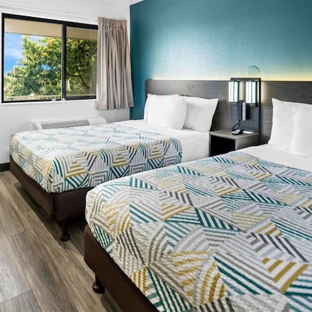 A hotel room with two beds, a nightstand, a lamp, and a window with curtains.
