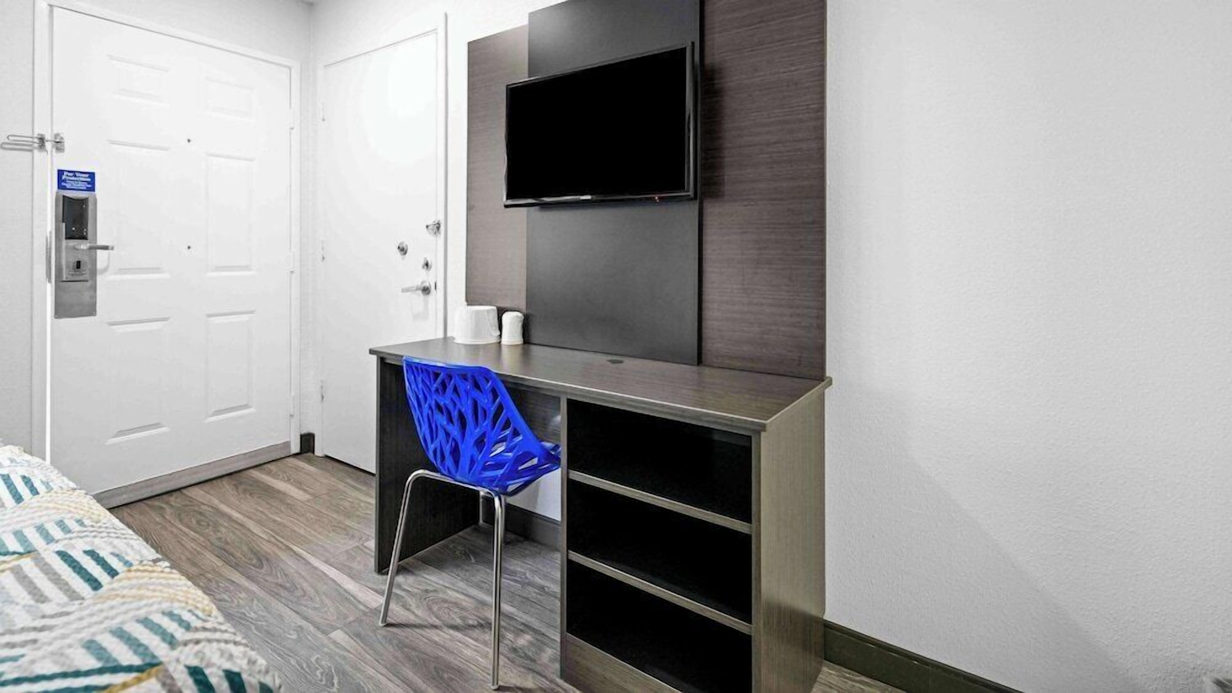 A hotel room with a desk, chair, TV, and a bed.