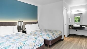 A hotel room with two beds, a nightstand, a wall-mounted lamp, a bathroom with a mirror, and a window.