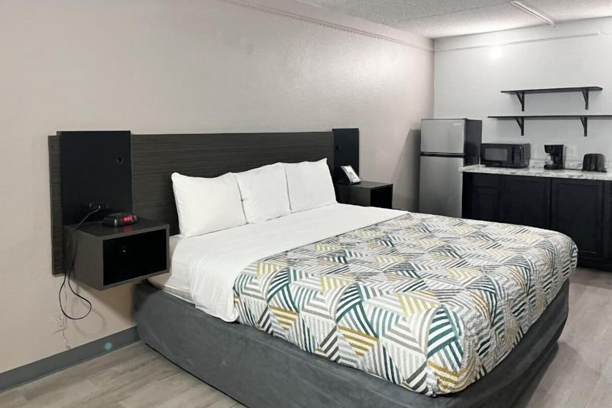 A modern hotel room with a bed, bedside tables, a built-in desk, a microwave, and a refrigerator.