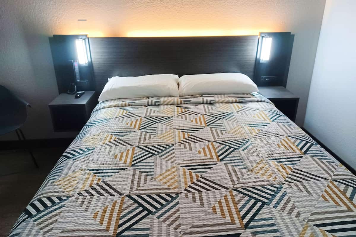 A hotel room with a bed, two bedside lamps, and a chair.