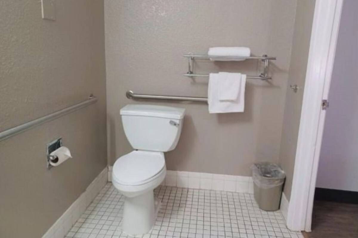 A small, clean bathroom with a toilet, a handrail, a towel rack, and a trash can.