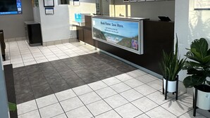 Una zona de recepción con pantalla digital, suelo de baldosas y plantas en macetas.