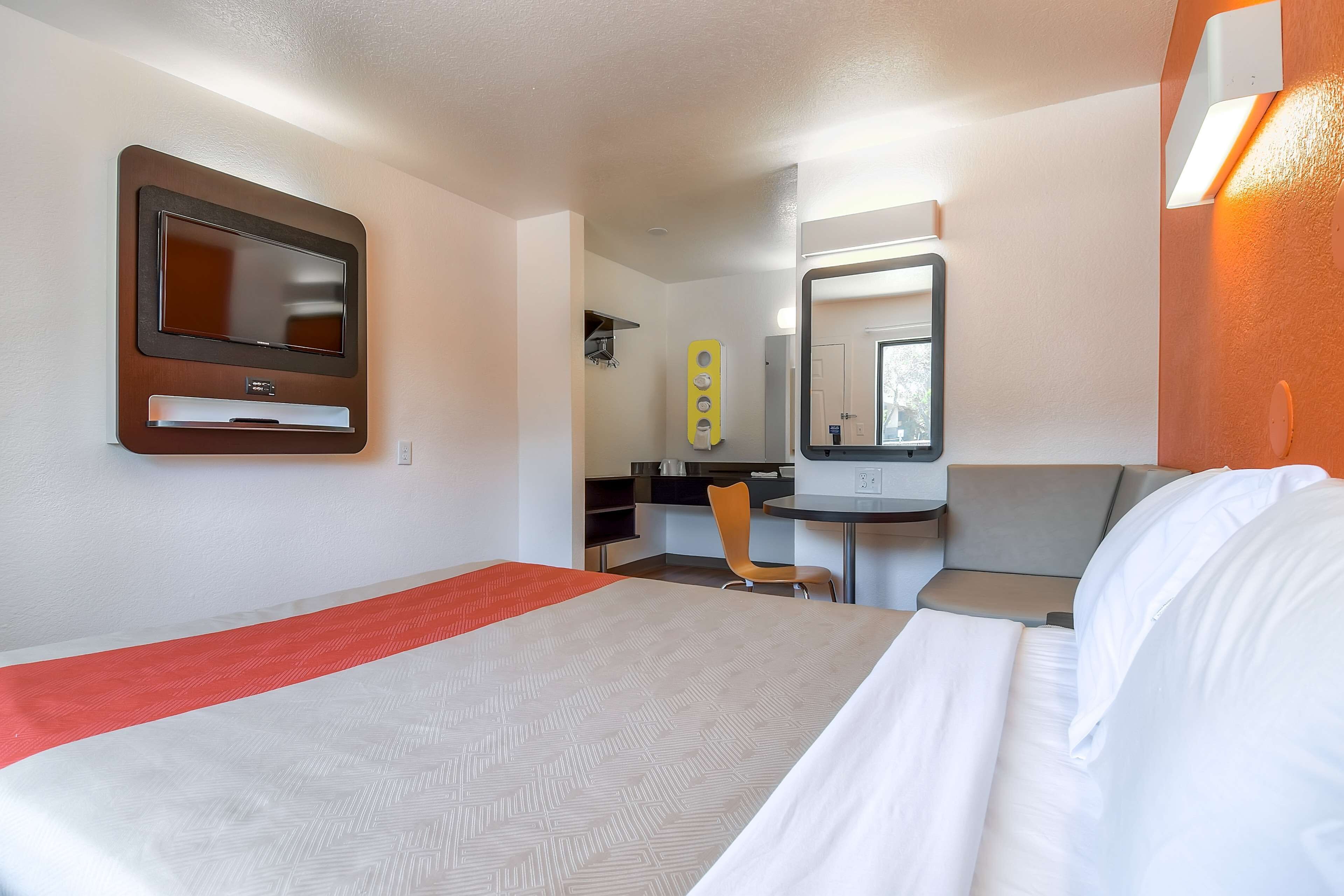 A hotel room with a bed, a desk, a chair, a TV, and a mirror.