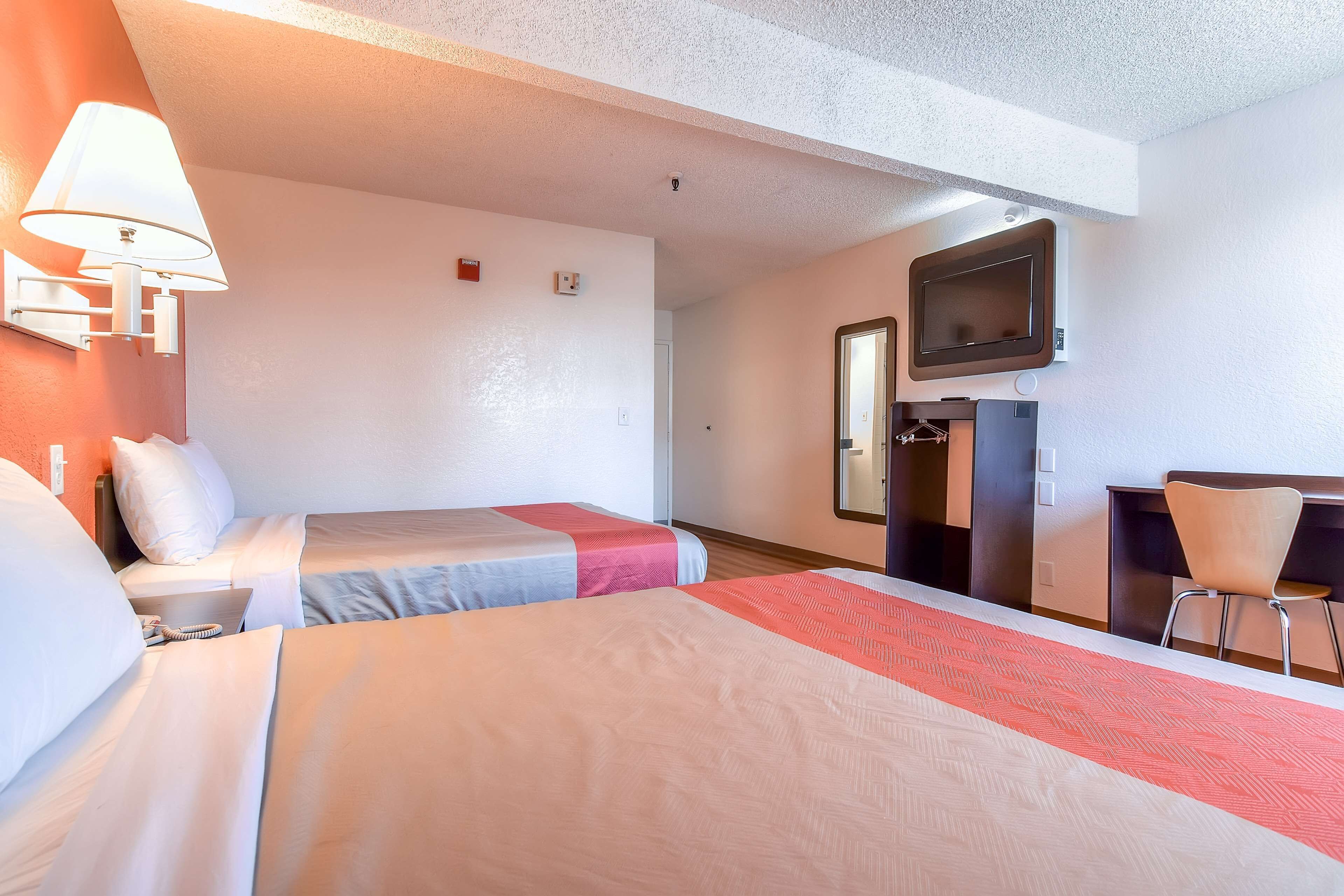 Una habitación de hotel con dos camas, un escritorio, una silla, un televisor y una lámpara.