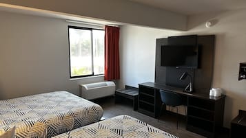 Habitación de hotel con dos camas estampadas, un escritorio con silla, un televisor de pantalla plana y una ventana con cortinas rojas.