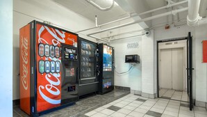 Zona de máquinas expendedoras con Coca-Cola y Blue Bunny, una cámara de seguridad y un ascensor.