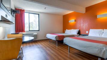 A hotel room with two beds, a dining table, and a window with red curtains.