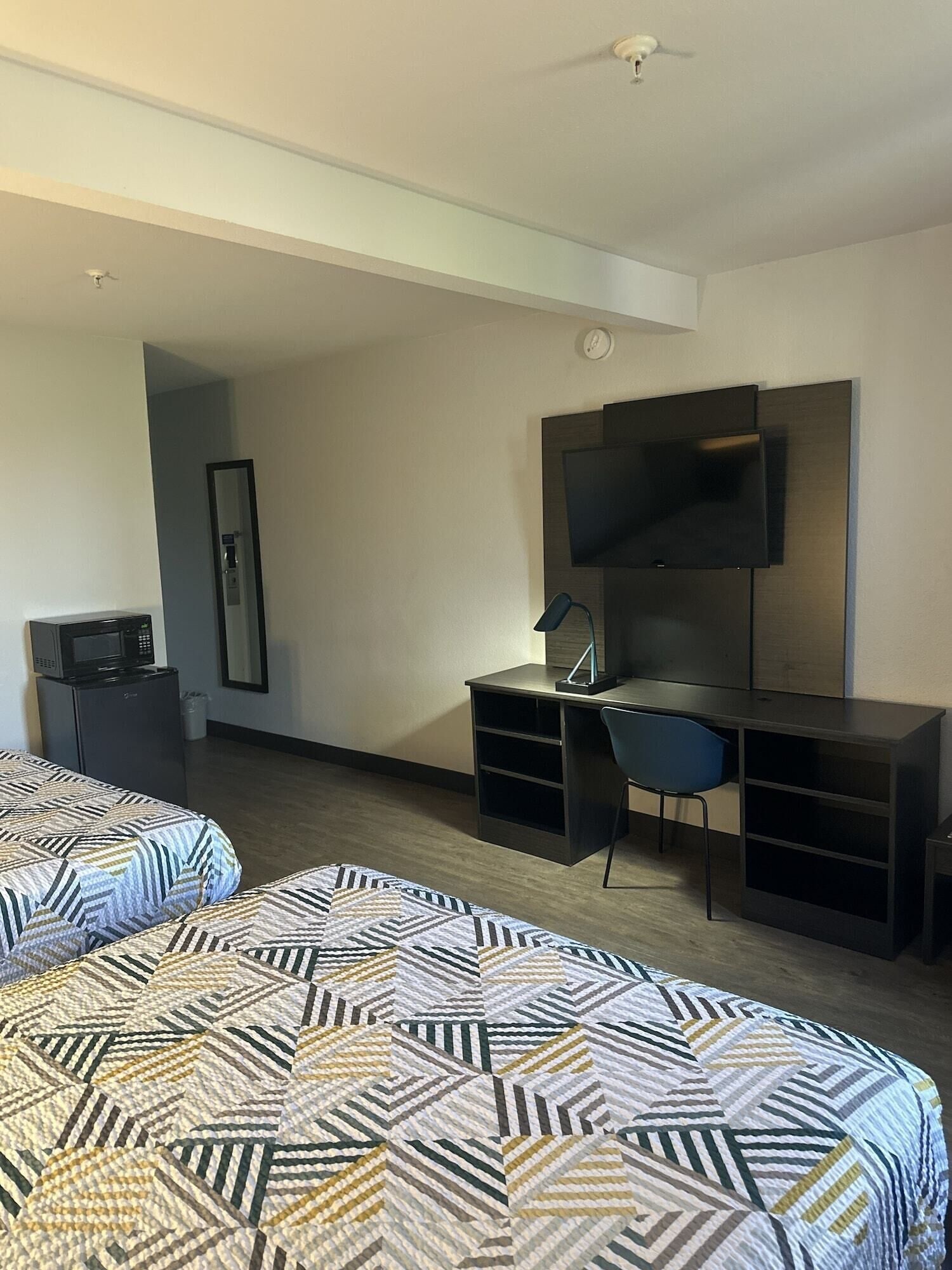 A hotel room with two beds, a desk, a chair, a TV, and a microwave.