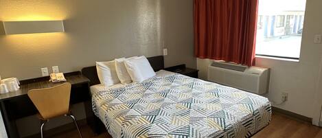 A hotel room with a bed, a desk, a chair, a window with curtains, and a wall-mounted heater.