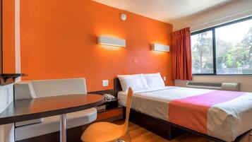 Una habitación de hotel con cama, escritorio, silla y ventana con cortinas.