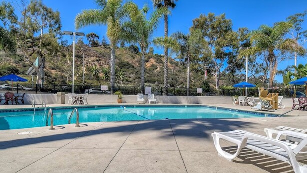 Una piscina con sillones de descanso y sombrillas, rodeada de palmeras y un paisaje montañoso.