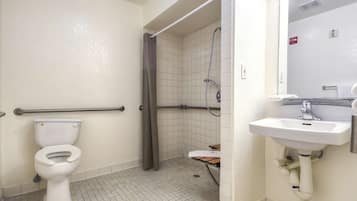 A bathroom with a toilet, a shower with a grab bar, and a sink with a mirror.