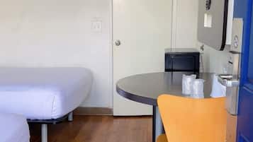 Une petite chambre d’hôtel avec un lit simple, une table ronde avec une chaise, un bureau avec un ordinateur et une porte.