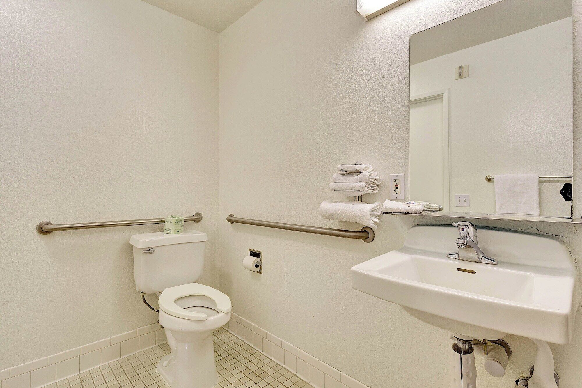 Un bany amb vàter, baranes, un lavabo i un mirall.