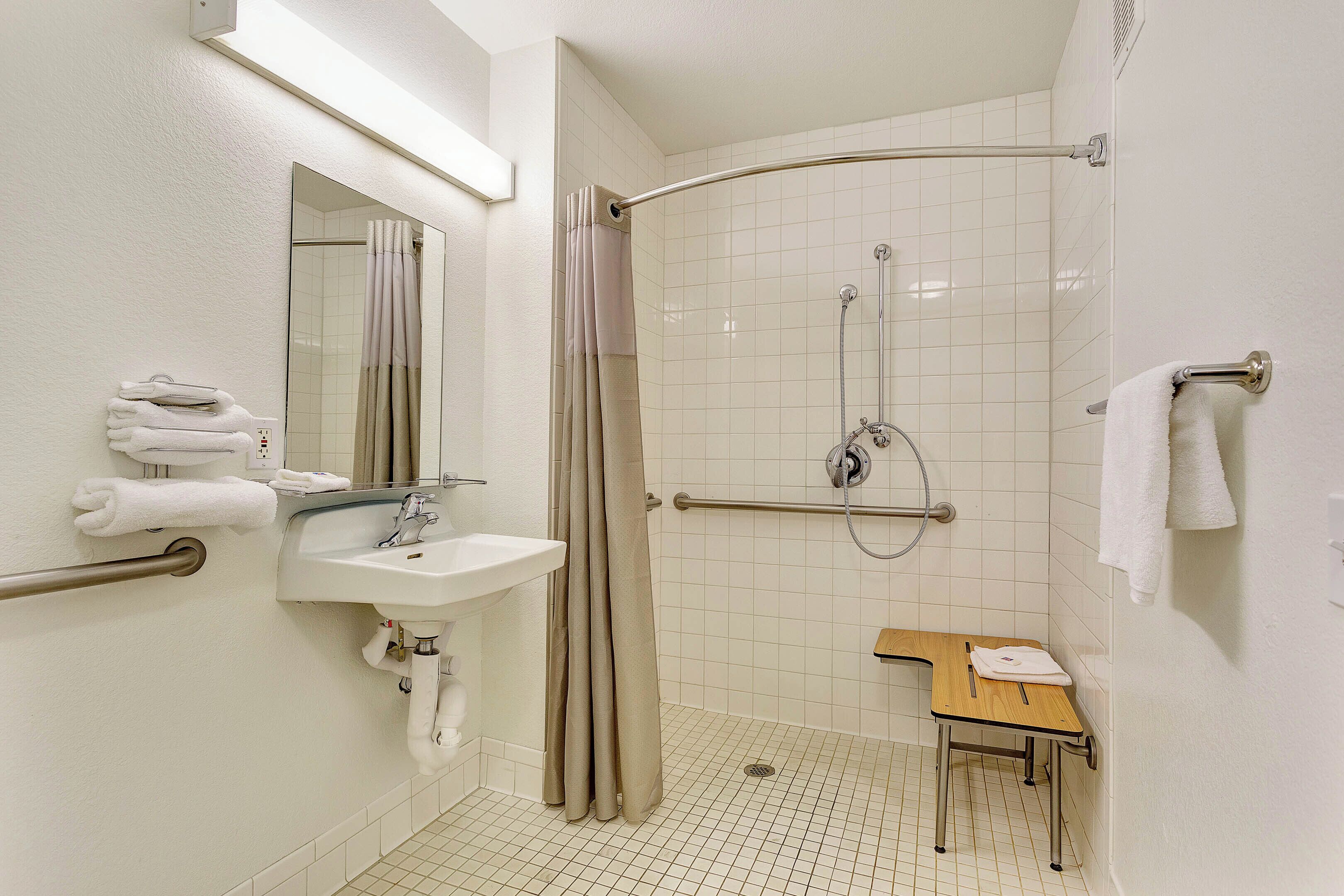 A bathroom with a shower, sink, and a small wooden table with a towel.