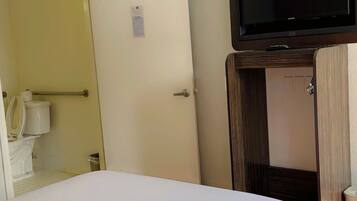A hotel room with a bed, a television mounted on a wooden stand, and a door leading to a bathroom.
