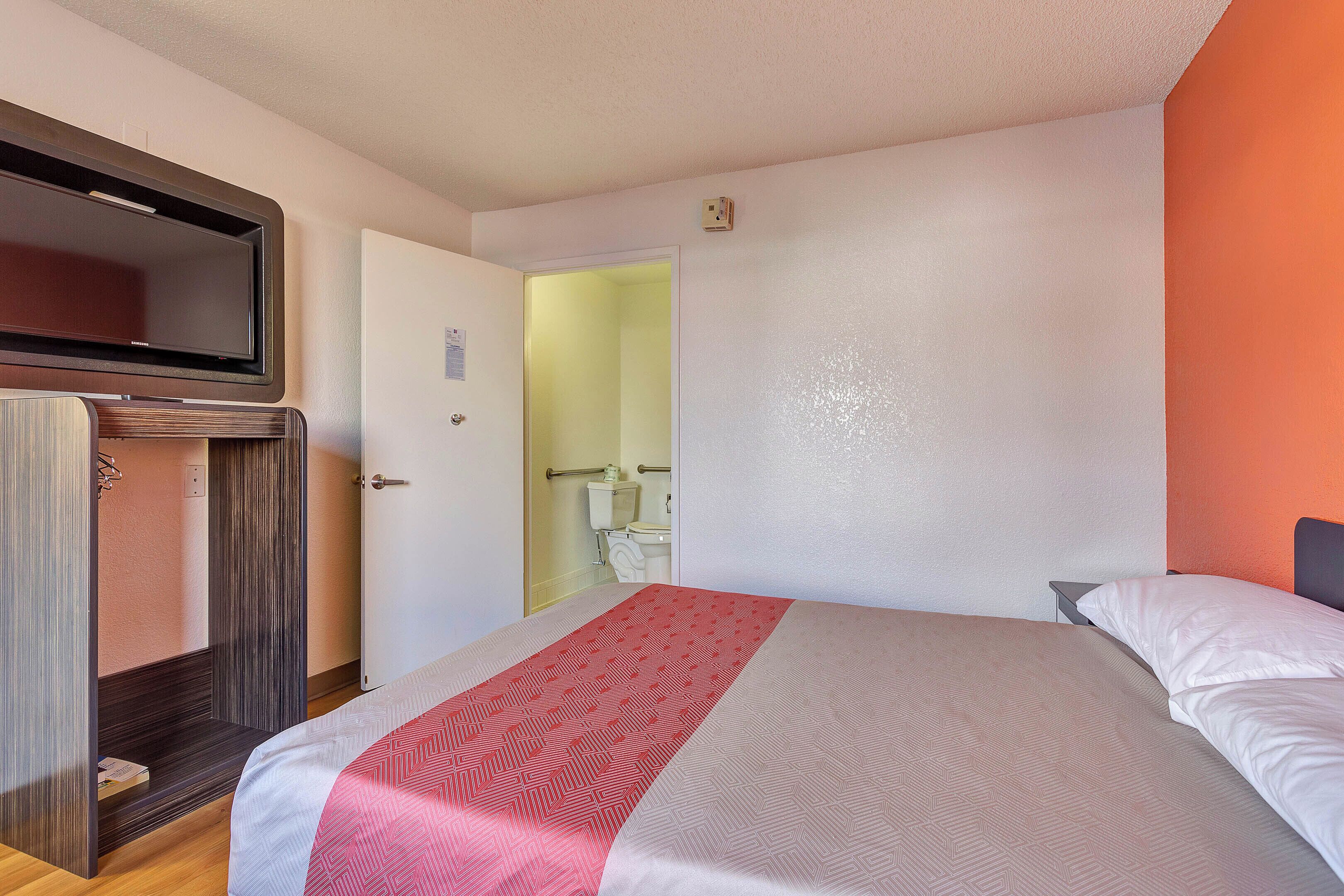 A hotel room with a bed, a TV mounted on the wall, and a door leading to a bathroom.