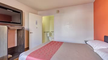 A hotel room with a bed, a TV mounted on the wall, and a door leading to a bathroom.