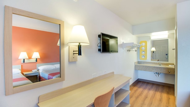 A hotel room with a bed, a desk, a chair, a television, a mirror, a lamp, and a bathroom with a sink and mirror. - Motel 6-Phoenix, AZ - East (Phoenix)