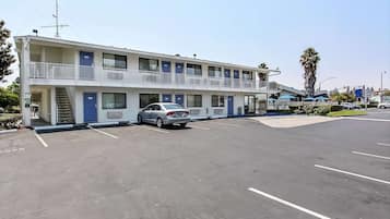 Un motel de dos pisos, un estacionamiento y un edificio de un solo nivel con una palmera al fondo.
