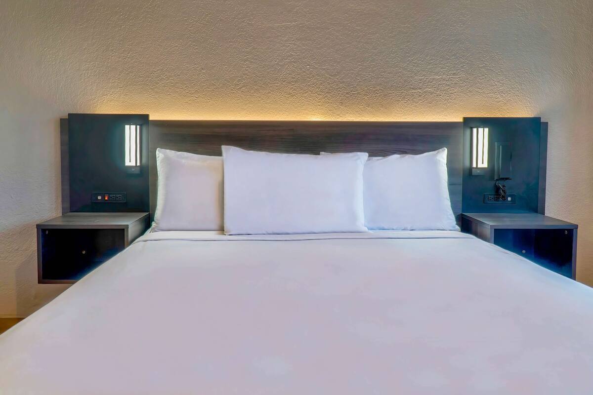 A neatly made bed with white linens and pillows, flanked by two bedside tables with built-in lighting.